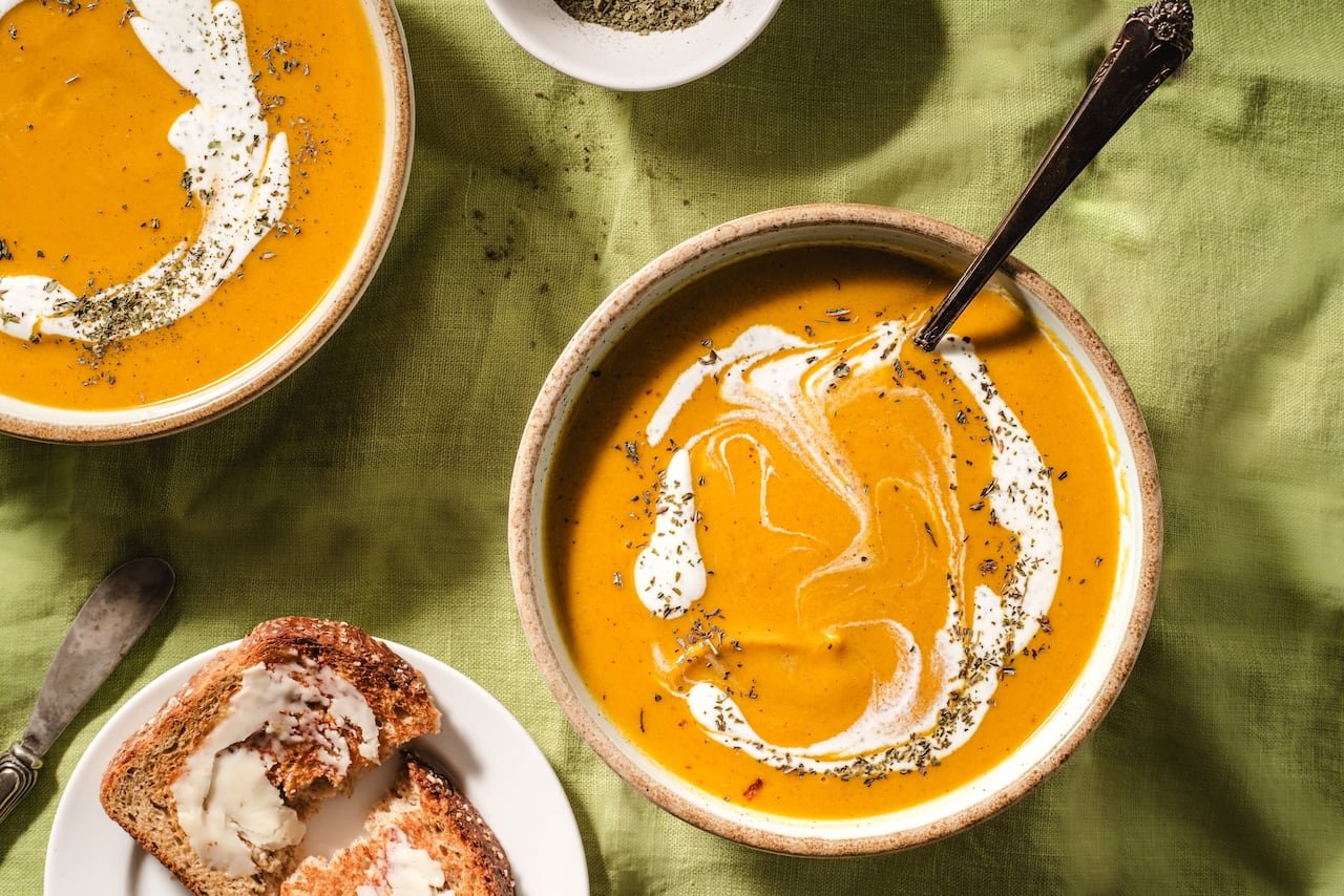 overhead view of 2 bowls of orange soup on a green tablecloth